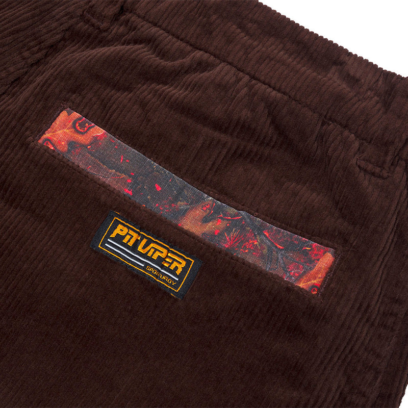 | detail_shot.JPG | Close-up of dark brown corduroy pants showing a decorative back pocket with a red and black patterned fabric strip and a black Pit Up! brand patch.
