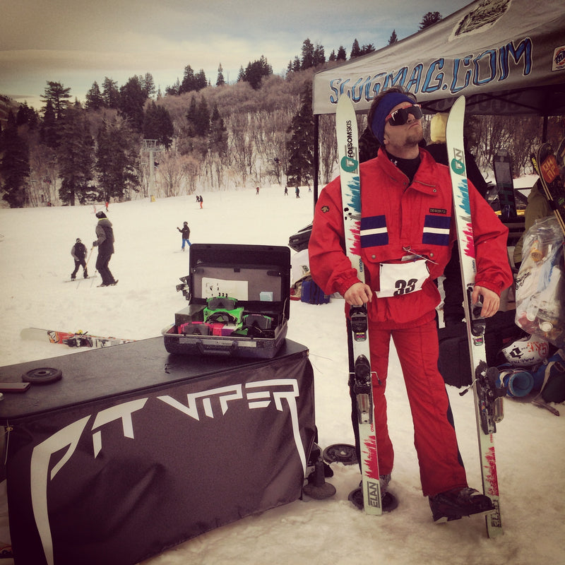 Person in red snow gear holding skis at a snowy outdoor event with 'Slugmag' and 'Viper' branding.