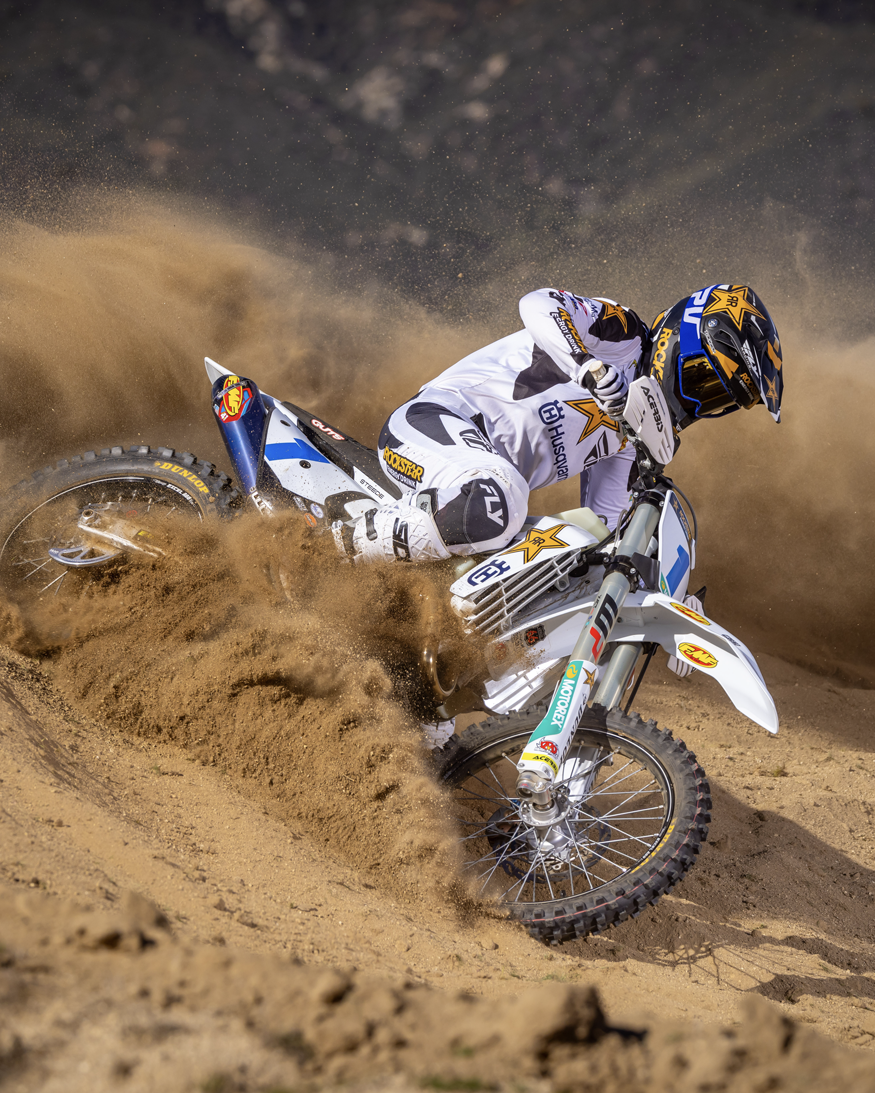 Motocross rider on a dirt bike kicking up dust in a desert setting