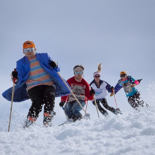 Four skiers in colorful outfits making a jump in the snow
