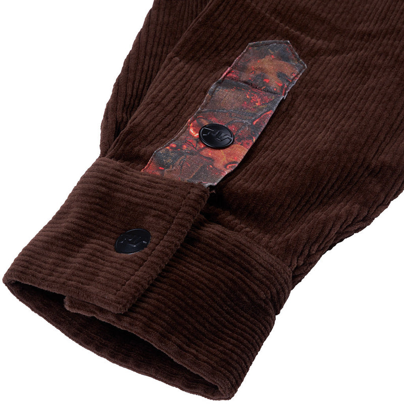 | detail_shot.JPG | Close-up of a brown corduroy jacket sleeve with a buttoned cuff and a decorative patterned fabric tab near the upper cuff, shown on a white background.