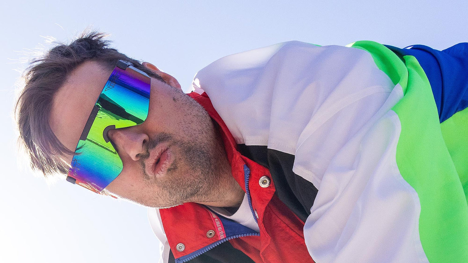 Person wearing colorful sunglasses and a multicolored jacket outdoors