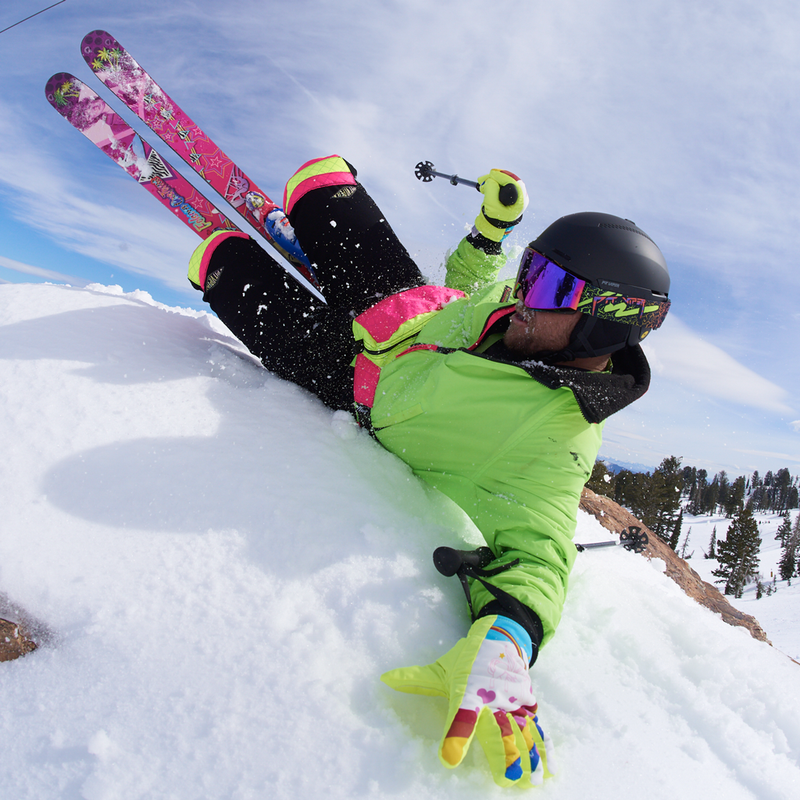 | layback.JPG | A skier lying on snow in a snowy outdoor setting, wearing a bright lime green ski jacket, black helmet, colorful ski goggles, black ski pants, and pink floral skis. 
