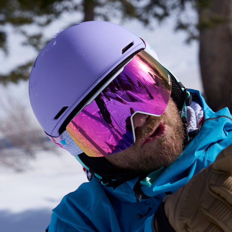 | chuck.JPG | A close-up of a person wearing a matte lavender ski helmet and large mirrored ski goggles with a pink-purple reflective lens, outdoors in the snow with trees in the background.