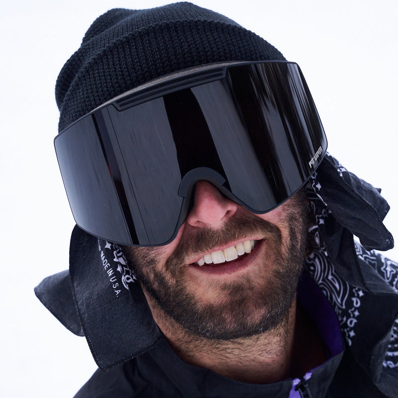 / Smoke | what.JPG | A close-up of a smiling man wearing black ski goggles, a black knit beanie, and a black bandana against a bright white background.