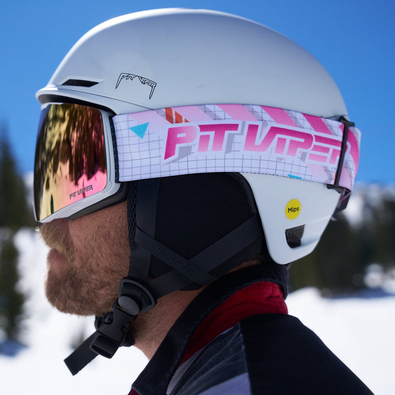 | chuck.JPG | A close-up side profile of a person wearing a white ski helmet with a pink and white patterned goggle strap and mirrored ski goggles, set against a snowy mountain background under a clear blue sky.