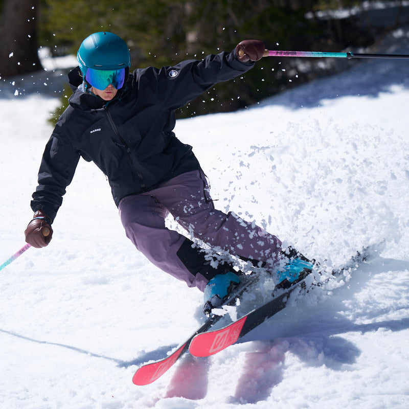 | sprayer.JPG | A skier carving through fresh powder on a snowy slope, wearing a black jacket, mauve-purple pants, a teal helmet, and bright pink skis, with ski poles extended.