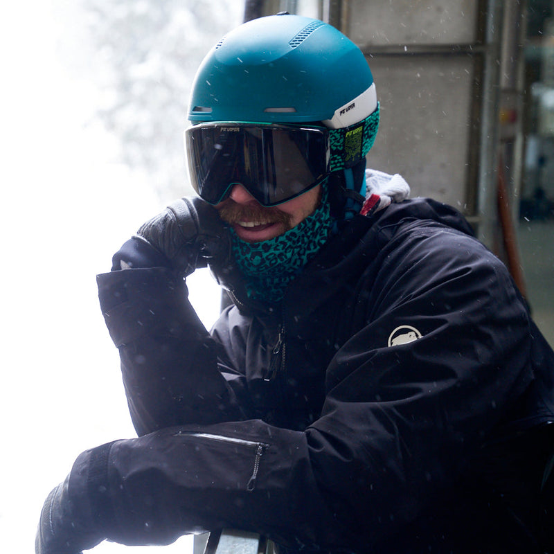 HDPV Smoke | tram_dave.JPG | A person wearing a teal ski helmet, dark ski goggles, a patterned teal neck gaiter, and a black ski jacket, posed outdoors in falling snow.