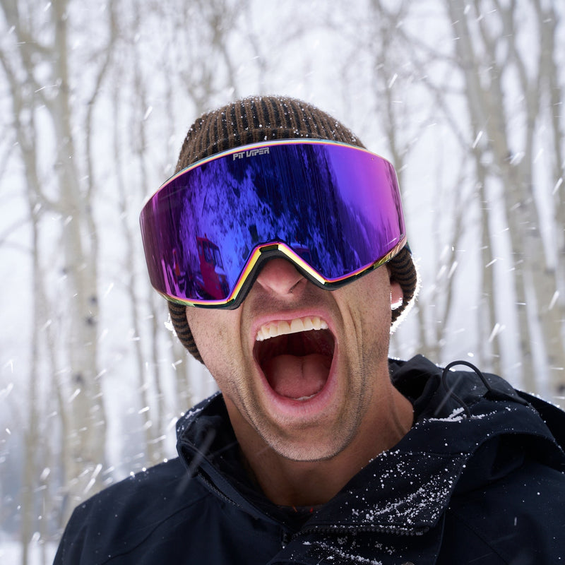 / HDPV Pink-Purple | why_yell_nick.JPG | A man wearing a brown knit beanie and a black winter jacket shouts with his mouth wide open while wearing large ski goggles with a purple and blue mirrored lens, set against a snowy background with bare trees.