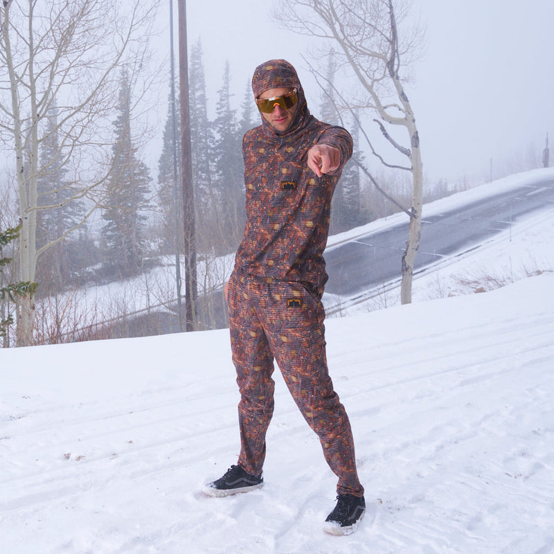 | nick_pointing_at_me.JPG | A man wearing a matching camouflage hooded sweatshirt and jogger pants stands in the snow, pointing toward the camera. The outfit has an abstract multicolor pattern in shades of brown, orange, and red, and he is wearing gold-tinted sunglasses.