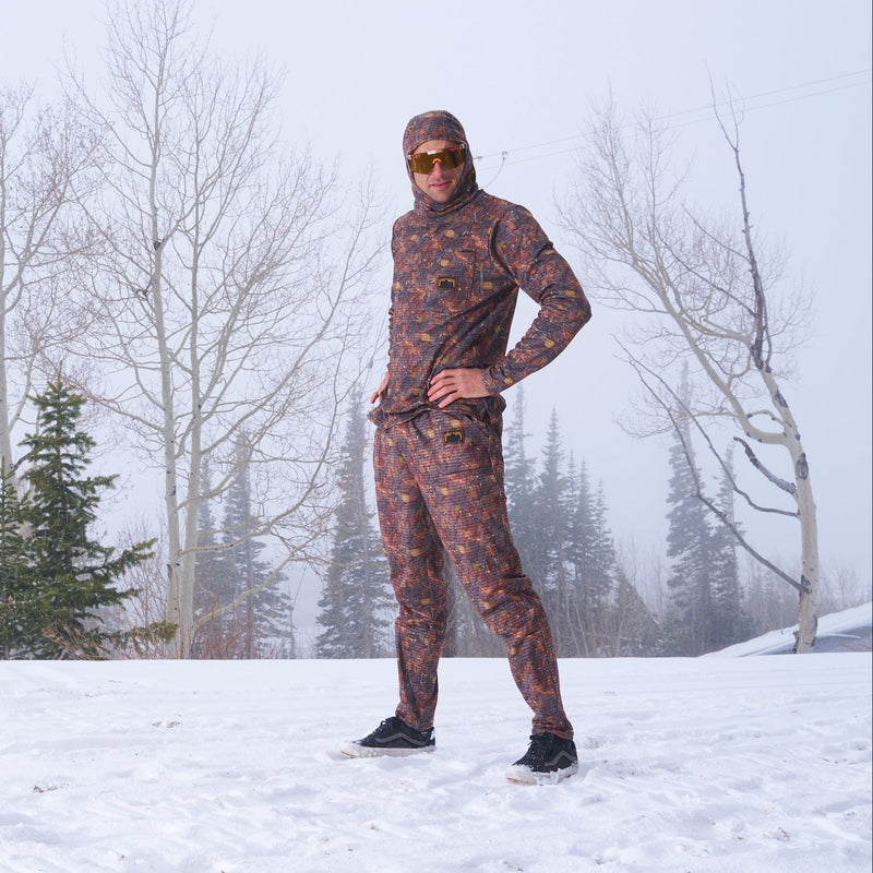 | nick_posing_for_u.JPG | A person standing in the snow wearing a full-body camouflage winter suit with a hood, black snow boots, and reflective sunglasses, with bare trees and evergreens in the background.