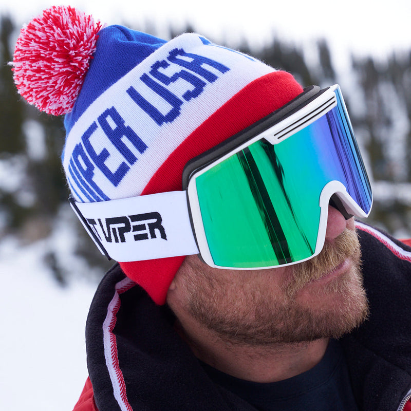 Blue-Green / Small | chuck_usa.JPG | A close-up of a person in a snowy outdoor setting wearing a red, white, and blue knit beanie with a pink pom-pom and large mirrored ski goggles with a green-to-blue reflective lens.