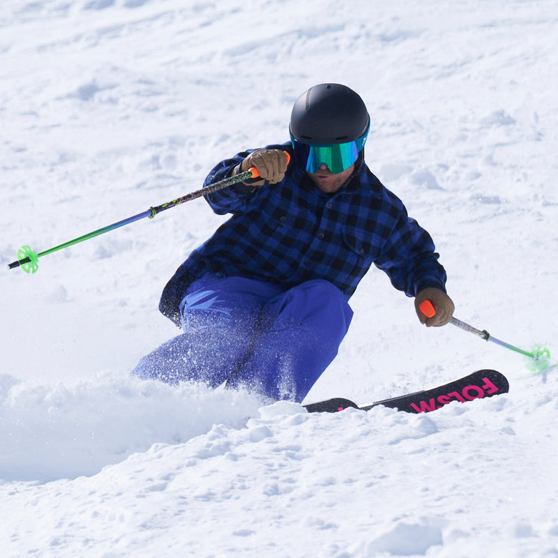 | drive_the_knee.JPG | A skier carving through fresh powder snow, wearing a blue and black plaid jacket, bright blue pants, a black helmet, and colorful ski poles.