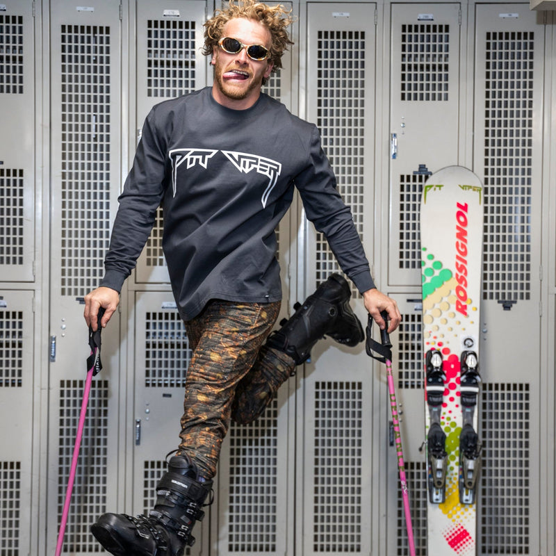 | photo_of_person.JPG |A man wearing sunglasses, a black long-sleeve T-Niner shirt, and camouflage ski pants poses in front of gray metal lockers, holding ski poles and standing next to a Rossignol ski.