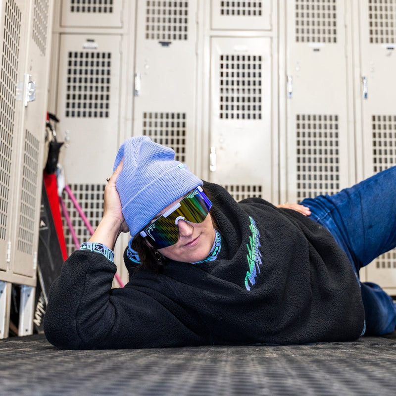 | photo_of_person.JPG | A person lying on a textured floor in front of metal lockers, wearing a light blue beanie, mirrored sunglasses, a black hoodie, and blue jeans.