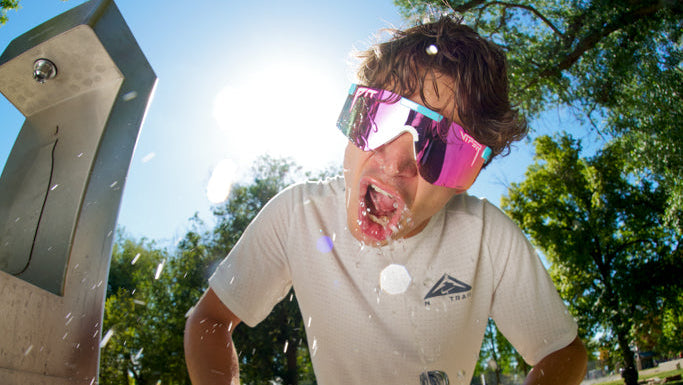 Person wearing reflective sunglasses outdoors with trees and clear sky in the background